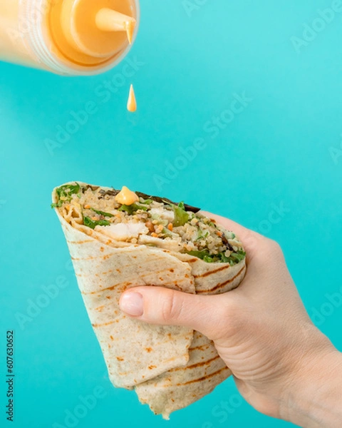 Fototapeta Chicken wrap in women hand seasoning with sauce on turquoise background