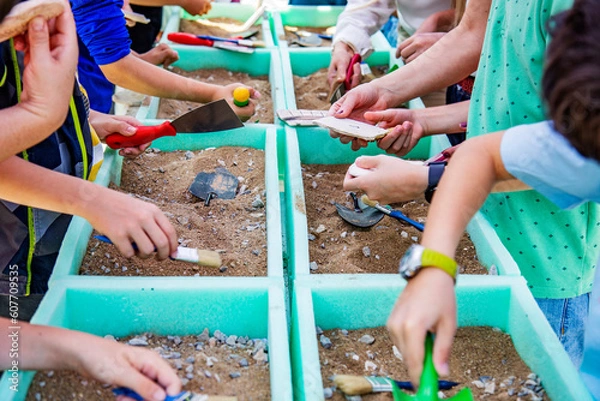 Obraz Children working as a archaeologists with brushes and shovels in containers with sand and stones, educations concept