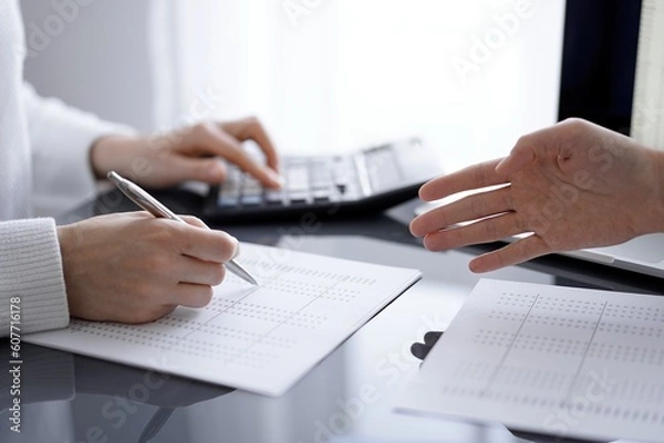 Obraz Woman accountant using a calculator and laptop computer while counting and discussing taxes with a client. Business audit concepts.