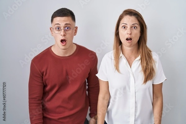 Fototapeta Mother and son standing together over isolated background afraid and shocked with surprise and amazed expression, fear and excited face.