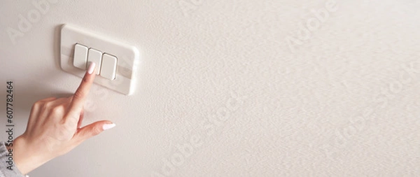 Obraz Female hand turning an electricity light switch on the wall.