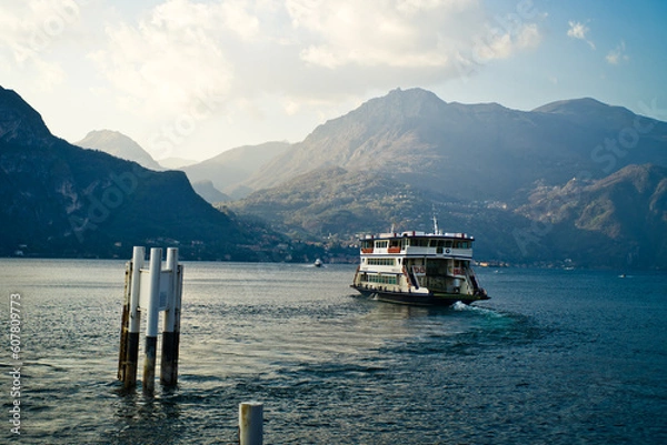 Fototapeta Lake Como from the shore of the town of Bellagio. View of the Alps mountains, buildings and a passenger ferry. Sunset