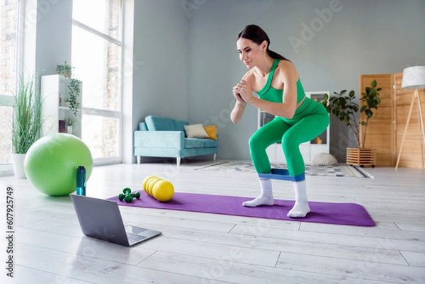 Fototapeta Full size photo of gorgeous great shape lady use rubber expander doing squats watch video netbook living room indoors