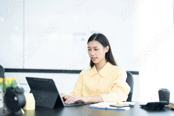 Fototapeta Portrait of pretty cheerful girl smiling while working on laptop in office