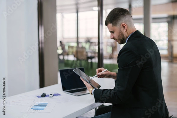 Obraz A man hold tablet and with checklist toy car on table and use laptop check online case of accident. Car insurance online concept.