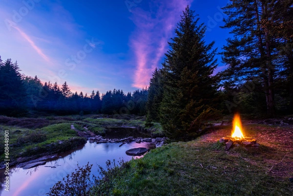Fototapeta In the Dolly Sods Wilderness in West Virginia, a campfire burns next to the Left Fork of Red Creek where the Blackbird Knob Trail crosses it. Pink clouds reflect in the water at sunset.