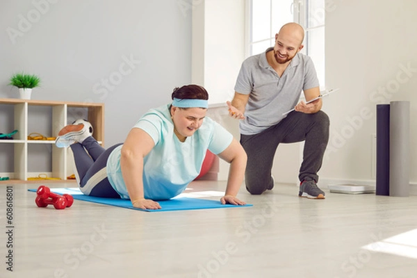 Obraz Obese, overweight woman working out with personal trainer in gym. Plus size, fat woman doing push up exercise under guidance of experienced male instructor. Sport, weight loss, healthy lifestyle