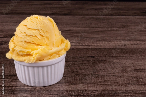Fototapeta Delicious yellow ice cream served in a white pot. Tasty traditional yellow gelato enjoyed around the world. Food on the left with space for texts on the right.