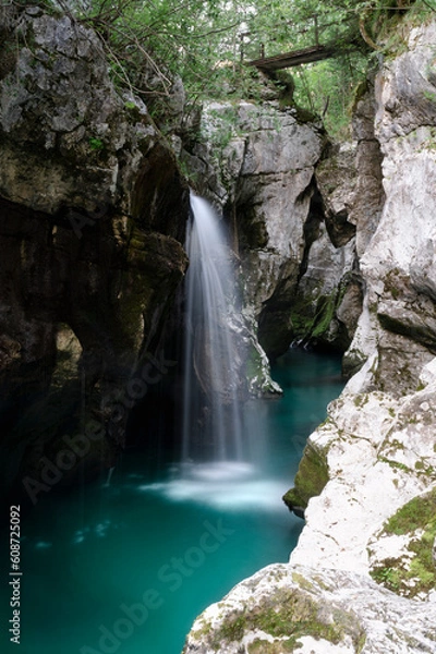Fototapeta Blurred image of a beautiful short waterfall in big gorge of the river Soca