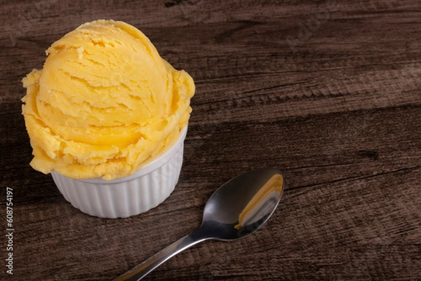Fototapeta Tasty yellow ice cream served in a white bowl next to a spoon. Gastronomic photography ice cream parlors and gelateries . Image with empty space on the right.