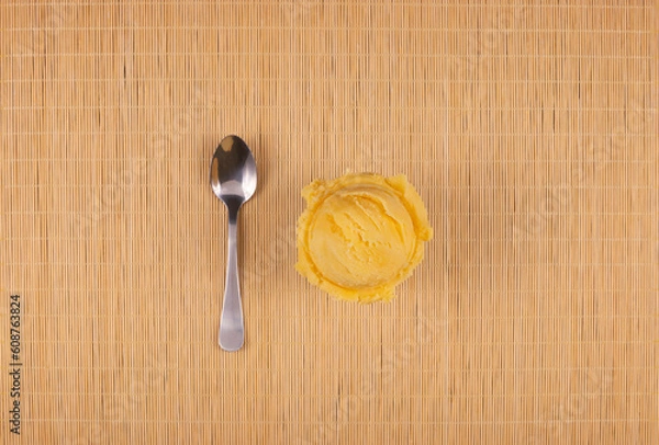 Fototapeta Tasty yellow ice cream served in a white bowl with a spoon on the side and a wooden background. Top view gourmet gelato photography.