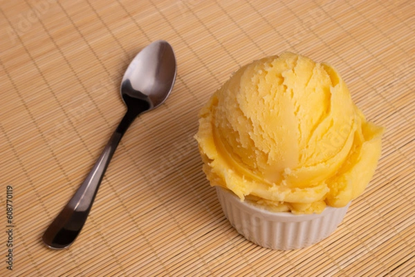 Obraz Yellow ice cream served in a white pot. Tasty traditional yellow gelato enjoyed around the world. Spoon tilted diagonally next to food. Close-up photography .
