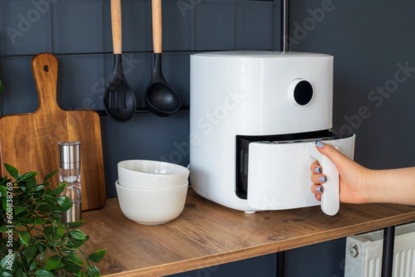 Fototapeta Woman at home using an air fryer. Making healthy food, frying without the use of oil.