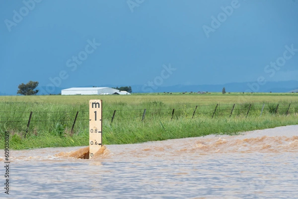 Fototapeta Close up of flood depth indicator on flooded road surrounded by water