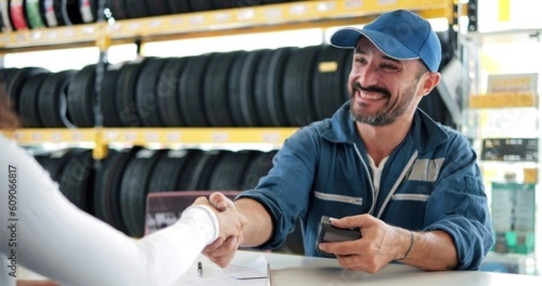 Obraz Happy automotive mechanic man in uniform shaking hands with client at auto repair shop. Car service, repair, maintenance, gestures and man mechanic concept