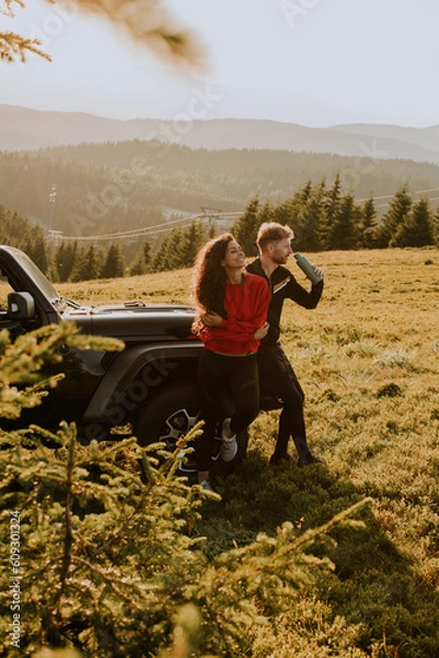 Obraz Young couple relaxing by a terrain vehicle hood at countryside