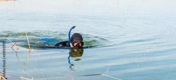 Fototapeta The diver swims in a wetsuit, flippers and a mask with a tube. The rescuer divers carries out work under water.