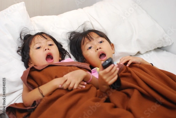 Obraz two beautiful Asian girls watching TV in the room while scared