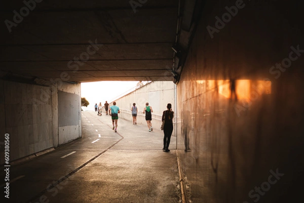 Fototapeta silhouettes of people walking and doing sports activities through a tunnel, tunnel with sunlight flares in the exit