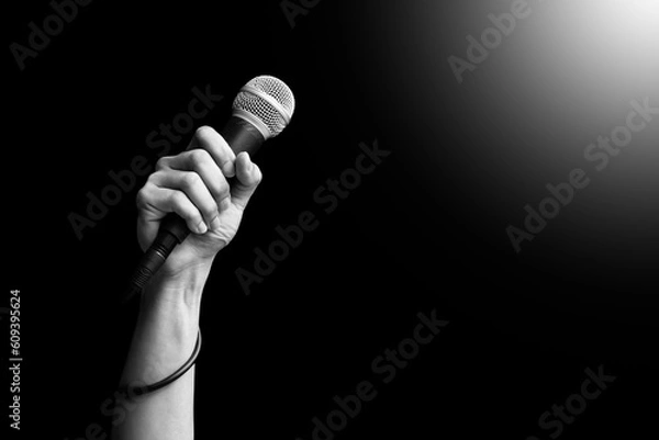 Obraz close up microphone in hand of singer raised his hand all the way up in live concert. singing concept. black and white