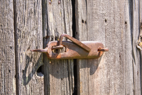 Fototapeta An old, original doorknob on a centuries-old wooden barn door in the harsh afternoon sun. Day.