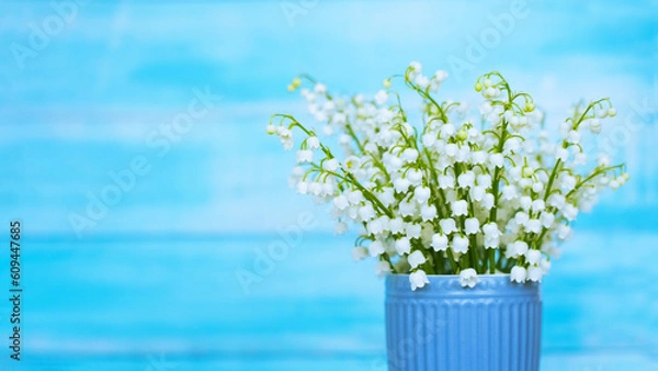 Fototapeta a bouquet of spring lilies of the valley in a blue vase on a blue background. bouquet of lilies of the valley close-up. background with lilies of the valley.