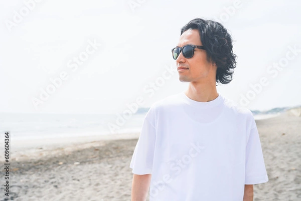 Fototapeta 夏の海岸を歩くサングラスをかけた男性