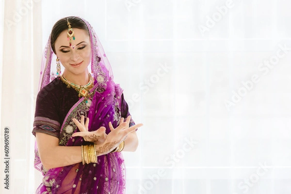 Obraz Pregnant woman in purple sari. mehendi. Indian painting on woman's hands and pregnant belly with henna tattoo on white room background