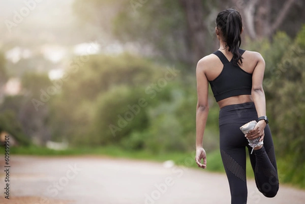 Fototapeta Nature, woman and warm up from back, workout motivation and fitness while stretching legs. Dedication, commitment and girl runner standing on road with leg stretch for outdoor run and exercise goals.