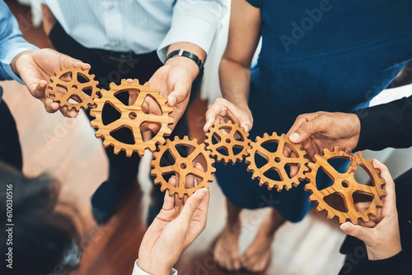 Fototapeta Office worker holding cog wheel as unity and teamwork in corporate workplace concept. Diverse colleague business people showing symbol of visionary system and mechanism for business success. Concord