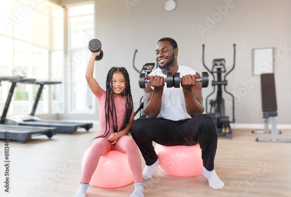 Fototapeta Father teaches, trains daughter to lift dumbbells, cute, smiling, cheerful and happy.