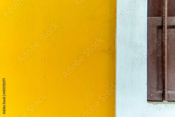 Fototapeta Zoom in on a yellow wall with a half wooden window reveals the fine details in the worn wood which gives a welcoming atmosphere