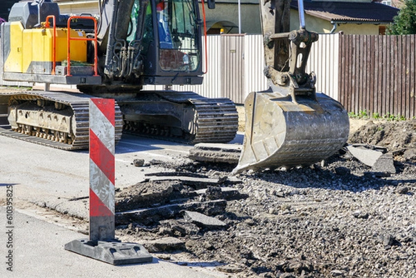 Fototapeta Crawler excavator with a bucket dismantle the asphalt before the reconstruction of the street