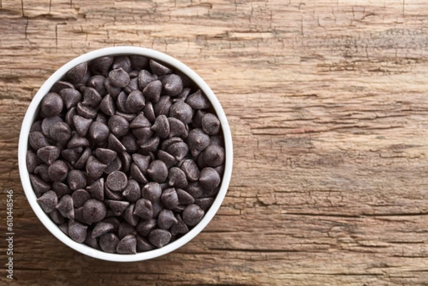 Fototapeta Chocolate chips or morsels in white bowl, photographed overhead on wood with copy space on the side (Selective Focus, Focus on the top chocolate chips)