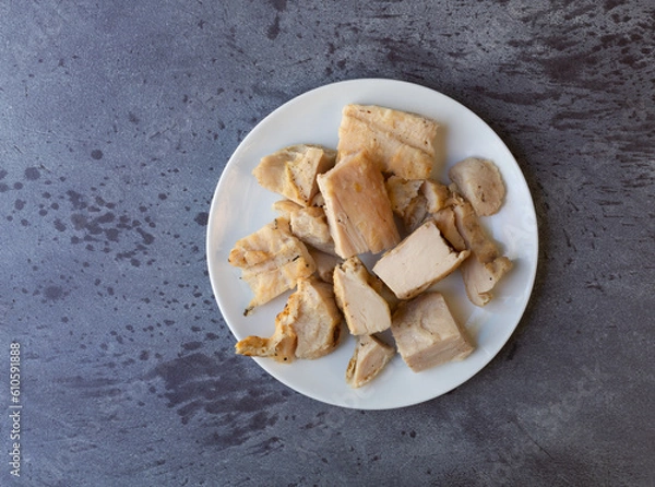 Obraz Top view of several pieces of roasted chicken breast on a white plate atop a gray mottled countertop.