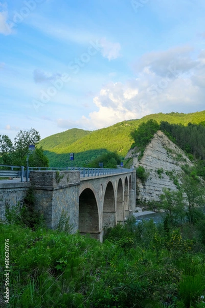 Fototapeta old bridge over the river Enza in Neviano degli Arduini, Parma, Emilia Romagna, Italy during the sunset light on the mountains