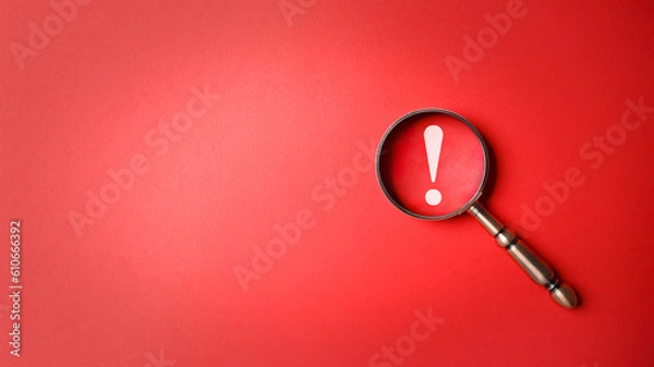 Fototapeta Magnifier magnifying exclamation mark on red background. Alert and precaution concept. Caution and risk management security signal announcement hazard and dangerous notice symbol
