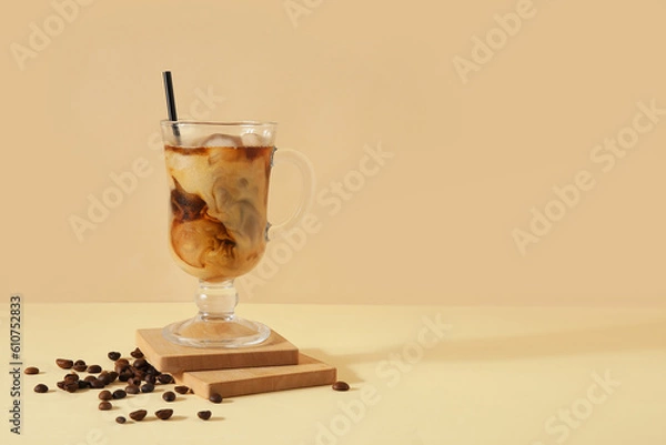 Fototapeta Glass of ice coffee with straw and beans on yellow table near beige wall