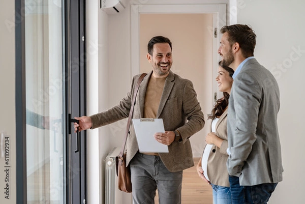 Fototapeta A young couple with a real-estate agent visiting an apartment for sale or for rent. Married couple buying an apartment. Real estate concept.