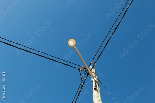 Fototapeta Street light in a wooden post with crossed cables and sky background..