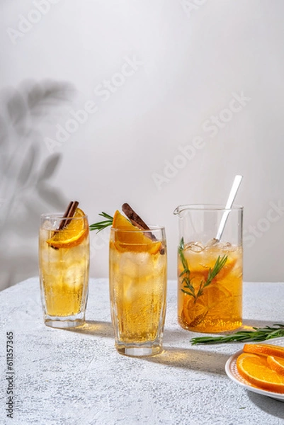 Fototapeta Fresh cocktail with orange, ice and herbs on the  table. Refreshing drink on a hot summer day. Ice tea. Sangria or punch in a glass