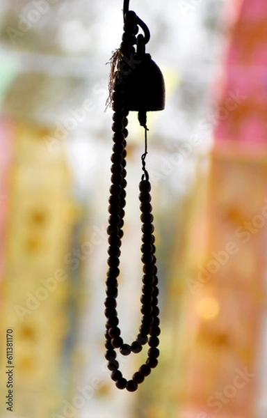Fototapeta A brown wooden rosary is hung from a golden bronze bell on a blurred background.