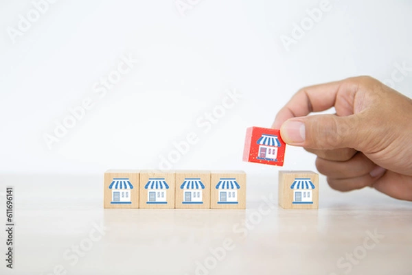 Fototapeta Franchise, Close-up hand choose cube wooden toy block stacked with franchises business store icon for business growth and branch expansion and bank loan.