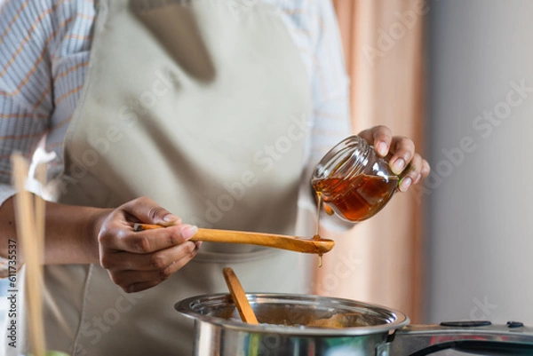 Fototapeta Female hands holding a bowl of bee honey and a wooden spoon. Close up. Elaboration of organic soap based on glycerin.