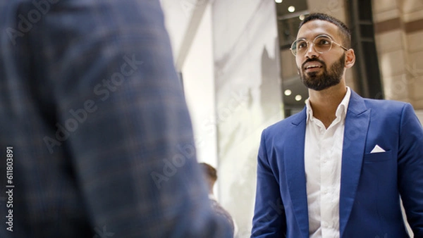 Fototapeta Handsome Indian professional in a smart suit speaks with somebody in a building lobby