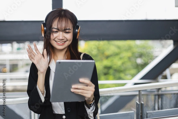 Obraz Asian beautiful female video conference calling on digital tablet wear headphones online app. Internet communication. Speak on video while commuting to work. lifestyle communication new generation.