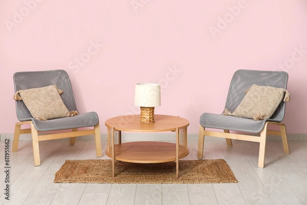 Fototapeta Armchairs with wooden coffee table, lamp and floor mat near pink wall