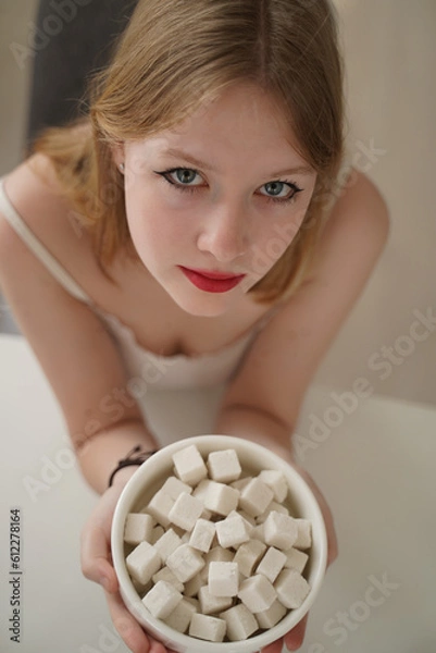 Obraz a large amount of sugar a young girl in a tank top sits in the kitchen in the morning and holds a large cup of sugar morning routine, pajama breakfast, day off