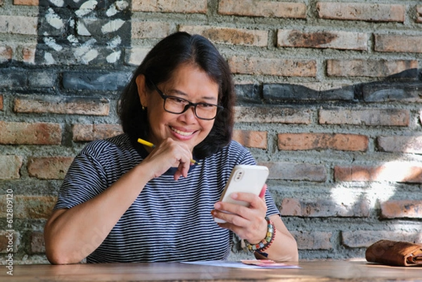 Fototapeta A middle-aged woman smiling cheerfully while looking at her smartphone
