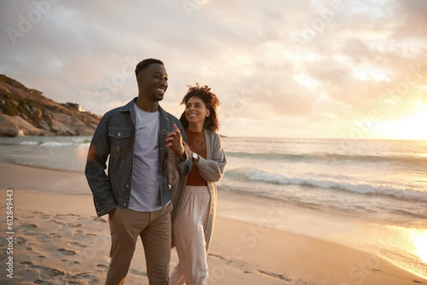 Fototapeta Smiling young multiethnic couple walking along a beach at sunset